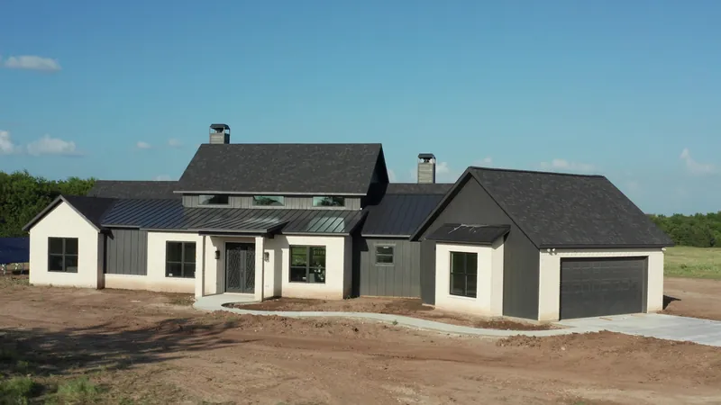 Three-quarter view of a newly completed custom home with standing-seam roof accents and curved walkway