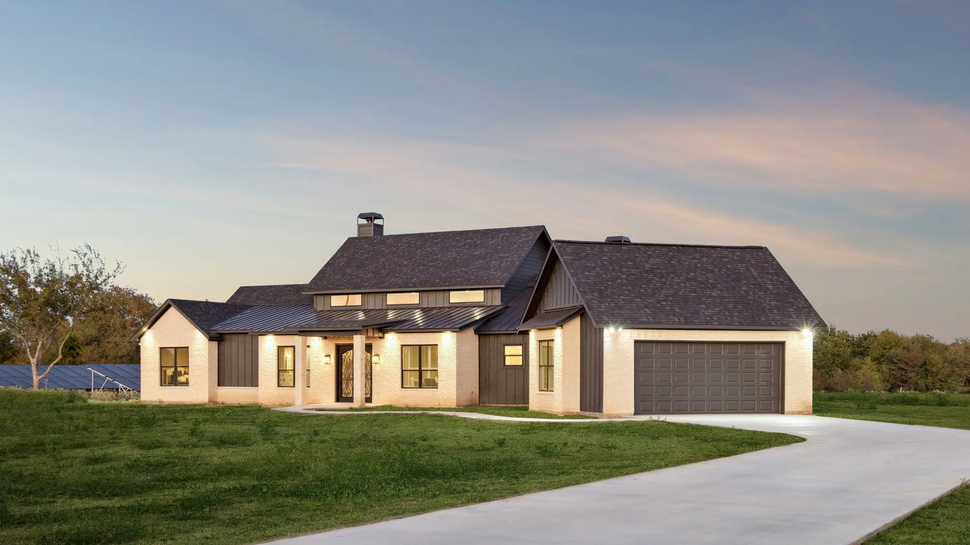 Ark Industries custom Texas estate home at twilight — white brick, board-and-batten accents, and a curving concrete drive across the lawn