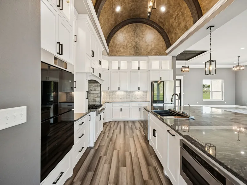 Custom kitchen with barrel-vaulted wood ceiling, white cabinetry, and granite island
