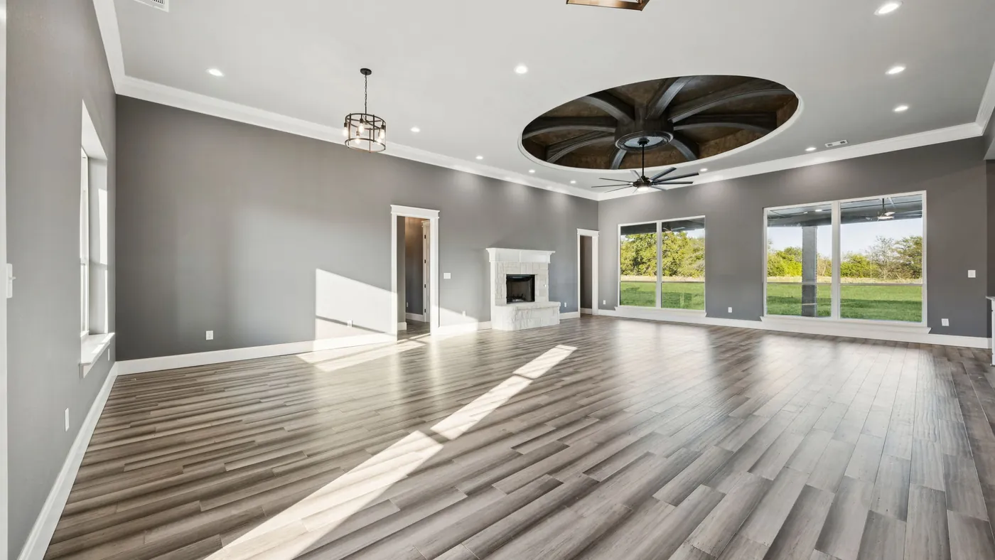 Great room of an Ark Industries custom home — stone fireplace, vaulted ceiling with sculpted fan, and tall windows over the pasture