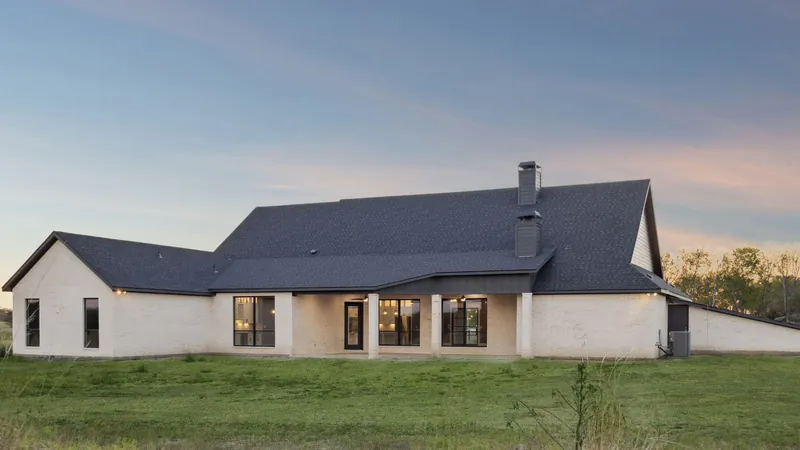 Rear elevation of a white brick Ark Industries home at sunset with covered back porch and lit interiors